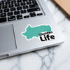 Teal Walden Life sticker with white border on laptop keyboard.
