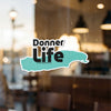 Sticker with "Donner Life" text and a turquoise irregular shape, on a glass window.
