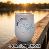 A white insulated tumbler with Lake Travis graphics sits on a wooden dock at sunset.