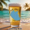 Glass of beer with "HAUSER LAKE IDAHO" text on beach with palm trees.