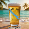 Glass of beer with "Camas Lake" and compass graphic on a beach.