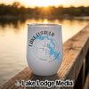 A white stainless steel wine tumbler with a compass and Lake Eufaula Oklahoma graphic stands on a wooden dock at sunset.