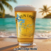 A pint glass of beer with a Lake Cumberland map design stands on a sunny beach.