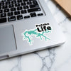 Patoka Life sticker with teal lake outline on laptop keyboard.