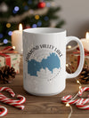 White mug with a blue Diamond Valley Lake map graphic and compass, on a wooden surface with holiday decorations.