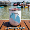 A white stainless steel tumbler featuring a blue Lake Almanor California graphic rests on a wooden boat deck with people swimming in the lake behind it.