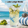 Glass with lime, mint, and ice on a beach with a sailboat in the background.