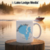 White mug with Sebago Lake Maine map design, steam rising, over a misty lake at sunrise.