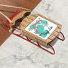 Wooden sled ornament with red metal runners and festive holiday message.